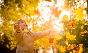 Child enjoying autumn time throwing leaves in the sun